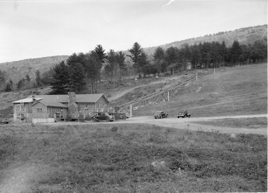 The newly-cut North Slope can be seen behind the base lodge in this photograph of Cranmore. The log walls of part of this building can still be seen in the main base lodge at Cranmore today.  Courtesy of North Conway Public Library 